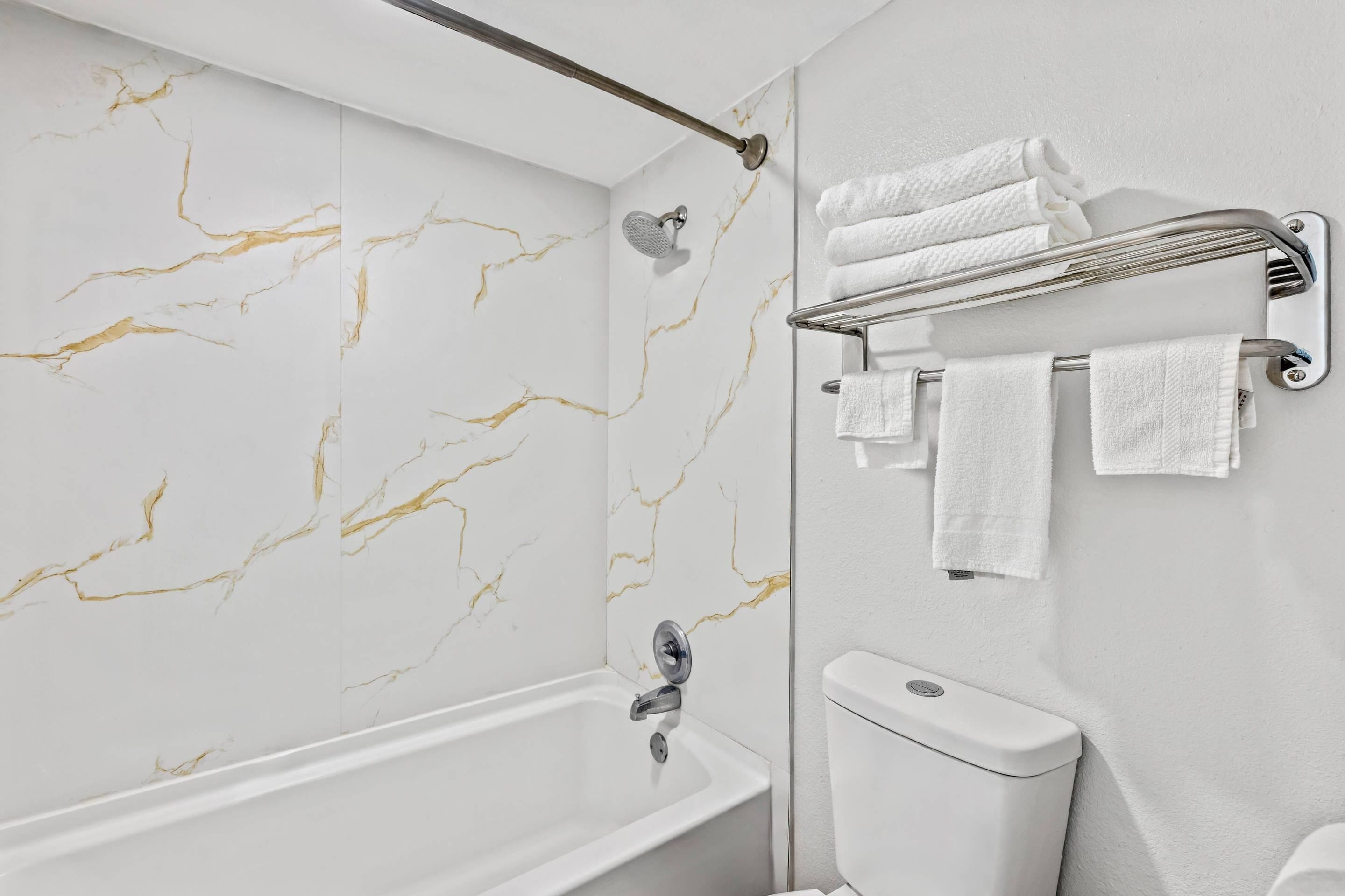 Une salle de bain avec un mur en marbre, une baignoire, des toilettes et un porte-serviettes avec des serviettes.