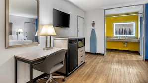 Habitación de hotel con escritorio, silla, televisión y baño visible a través de una puerta abierta.