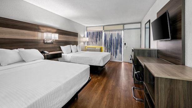 Habitación de hotel con dos camas, un escritorio, un televisor y una ventana con cortinas.