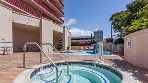 A pool area with a hot tub, outdoor seating, and a building with red railings. - Ramada by Wyndham San Diego National City (National City)