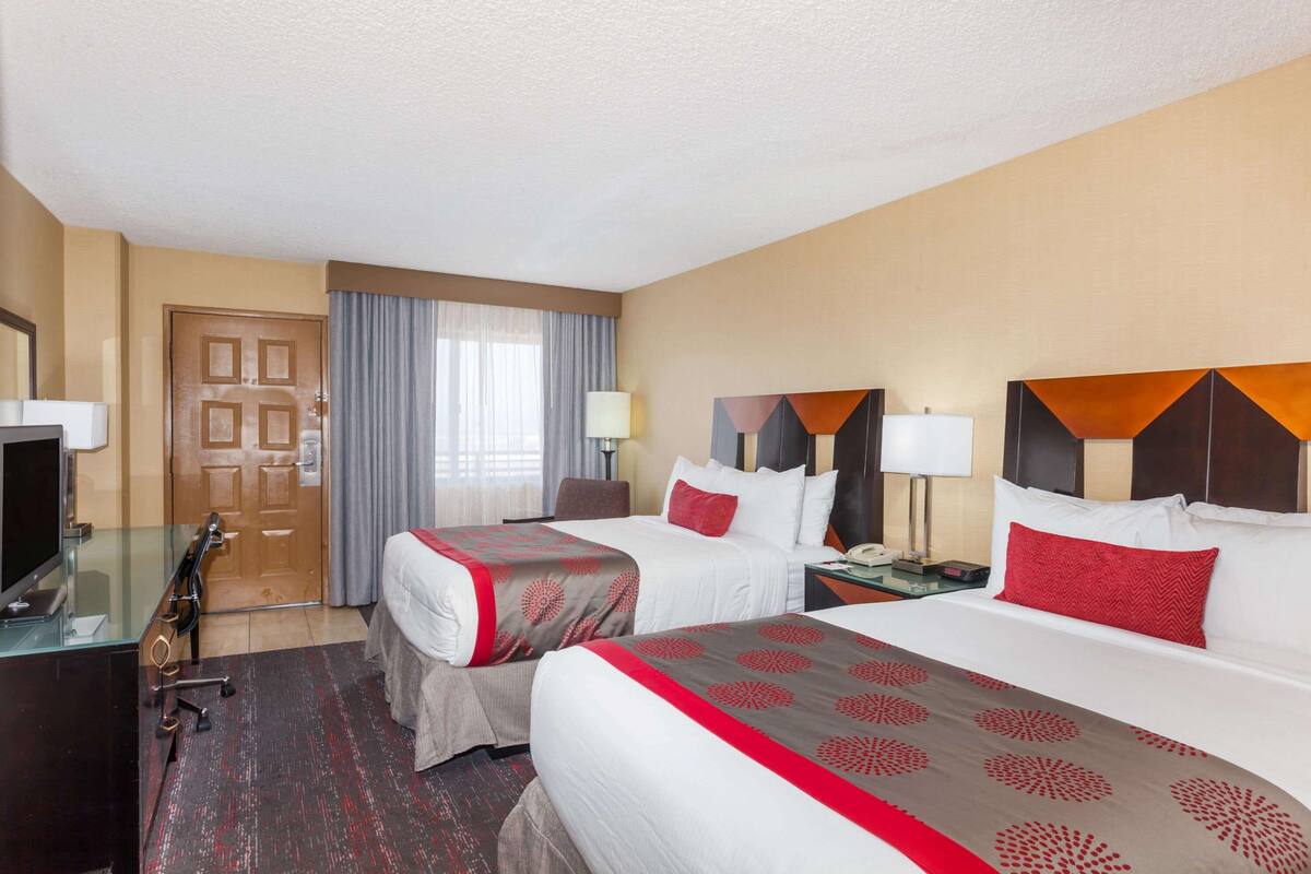 A hotel room with two beds, a desk with a computer, a TV, and a door.