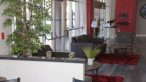 A modern living room with a sofa, a coffee table, and a red rug. There is a plant on the coffee table and a window with curtains. - Ramada by Wyndham San Diego National City (National City)