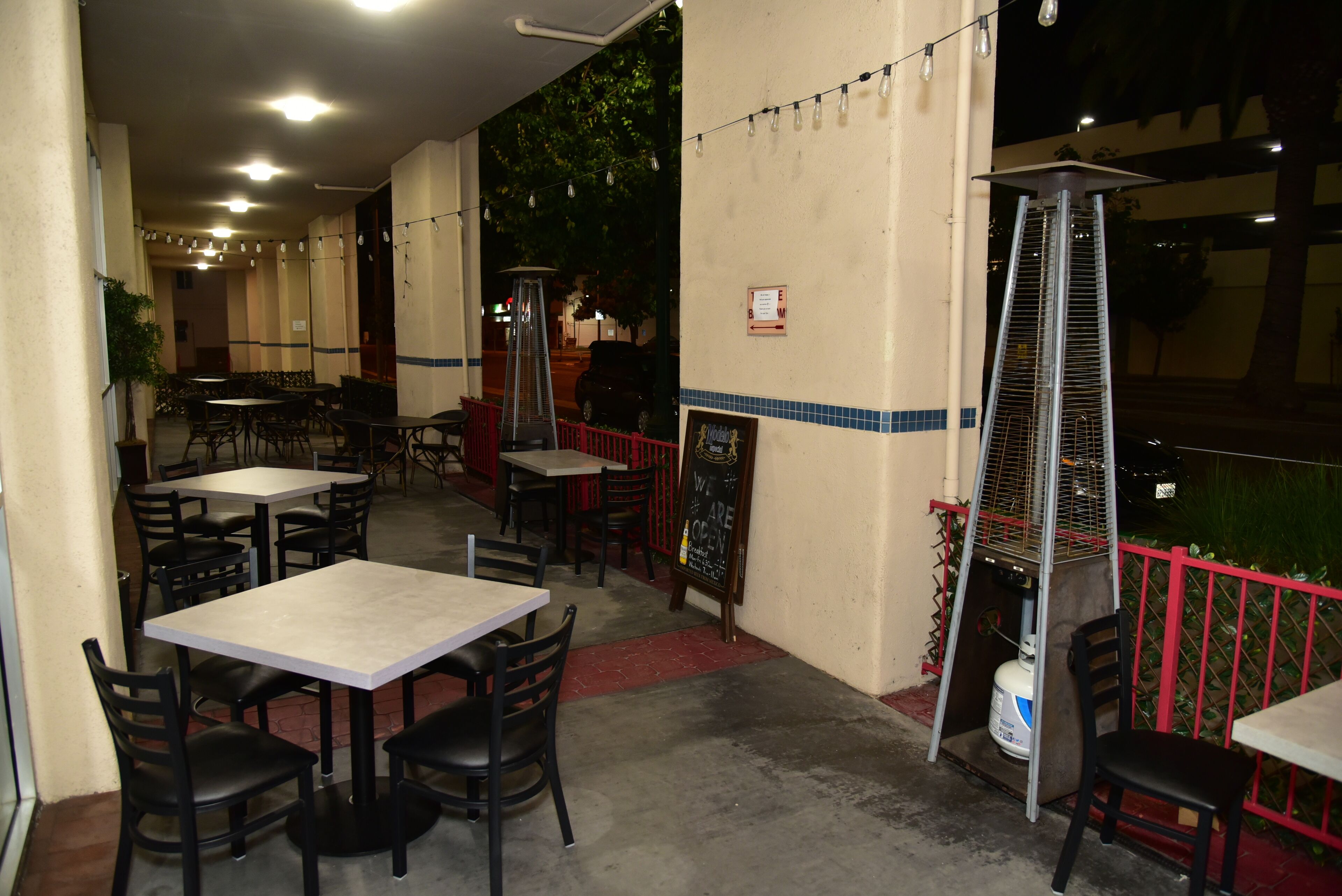 An outdoor dining area with tables and chairs, a red railing, and a chalkboard menu.