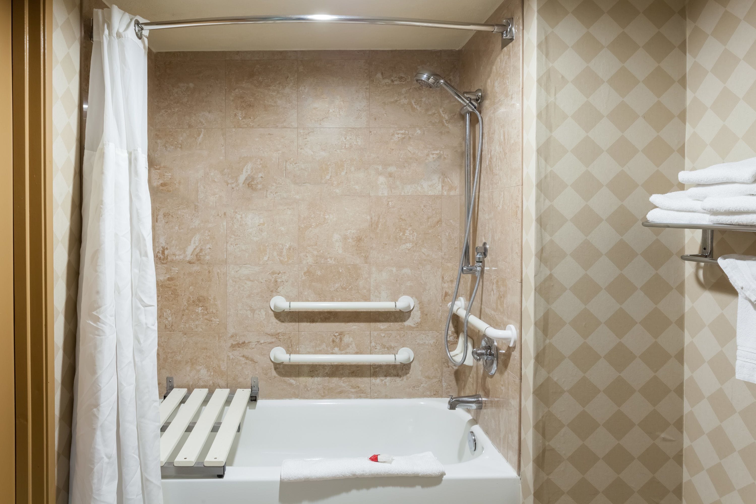A modern bathroom with a bathtub, shower, and handrails.