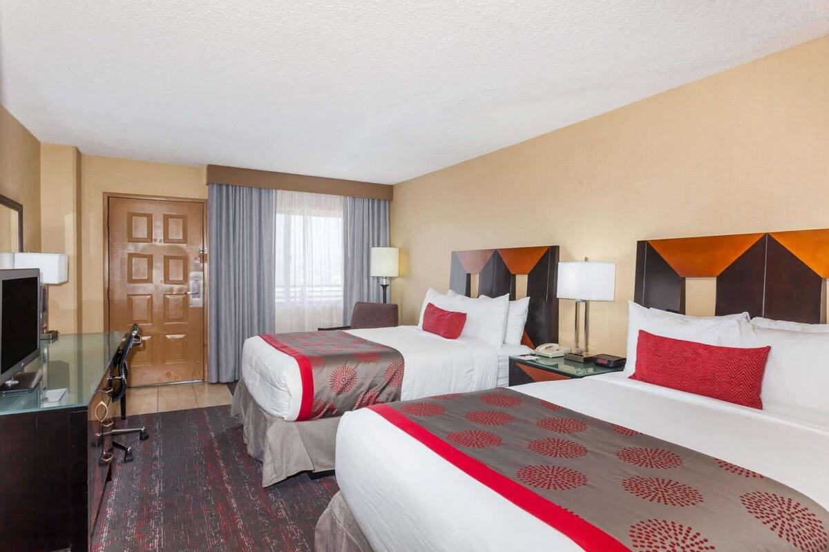 A hotel room with two beds, a desk with a TV, and a door.