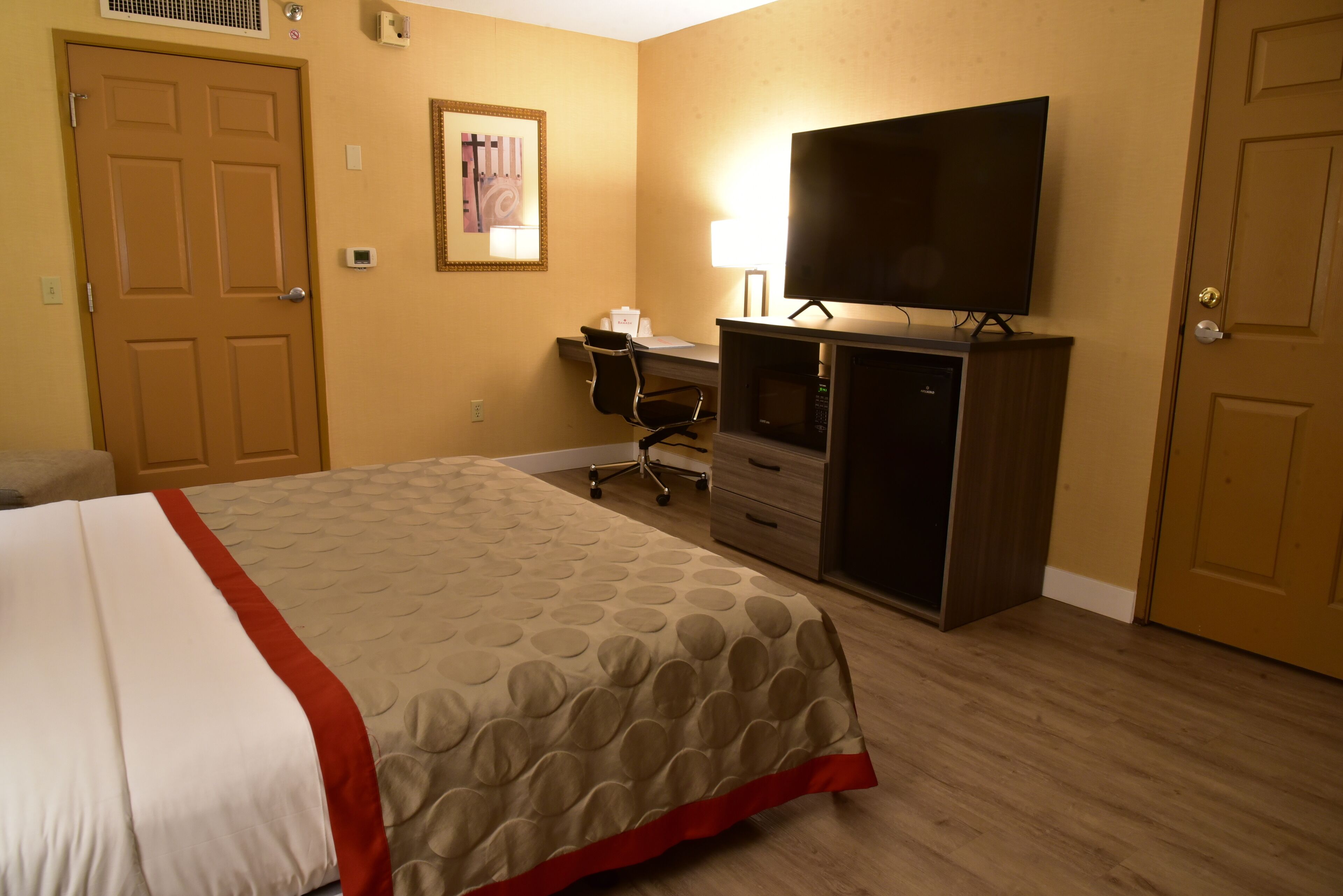 Una habitación de hotel con una cama, un escritorio con silla, un televisor y un armario.