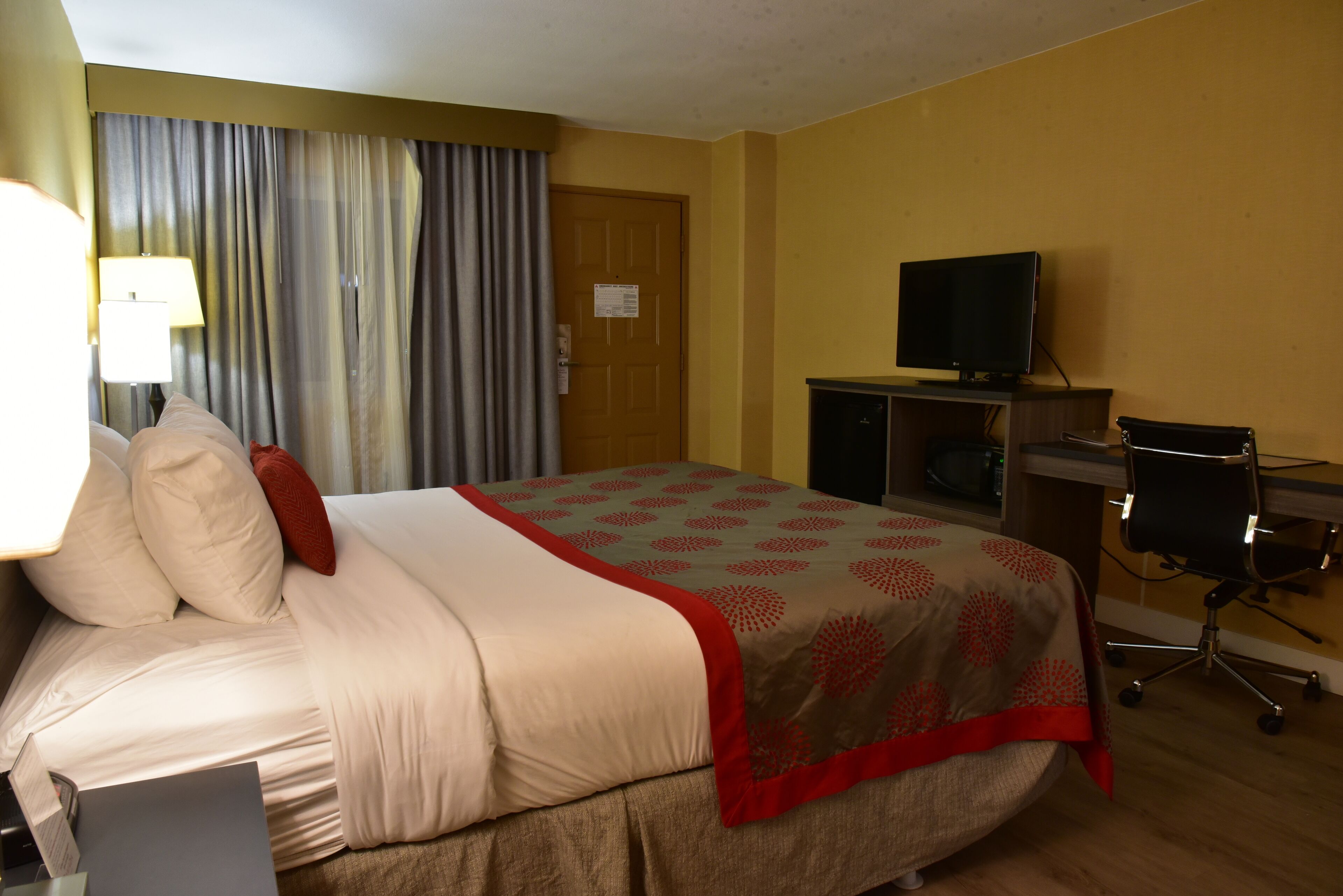 Una habitación de hotel con cama, escritorio, computadora, televisor y una silla.