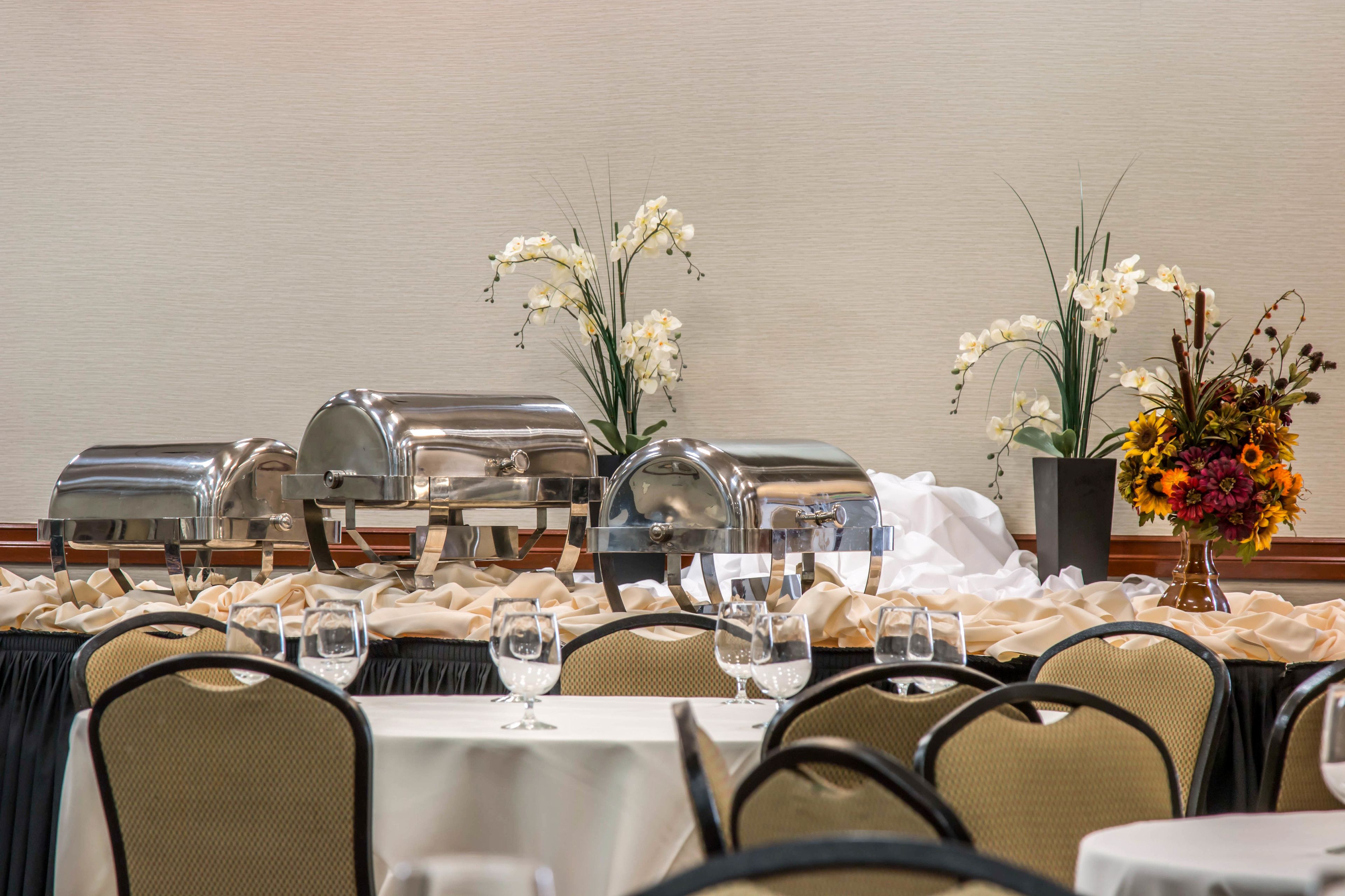 Een feesttafel gedekt met witte tafellinnen, zilveren buffetwagens en glazen.