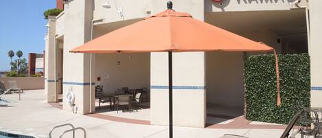 A poolside area with lounge chairs, an umbrella, and a sign for Ramada hotel.