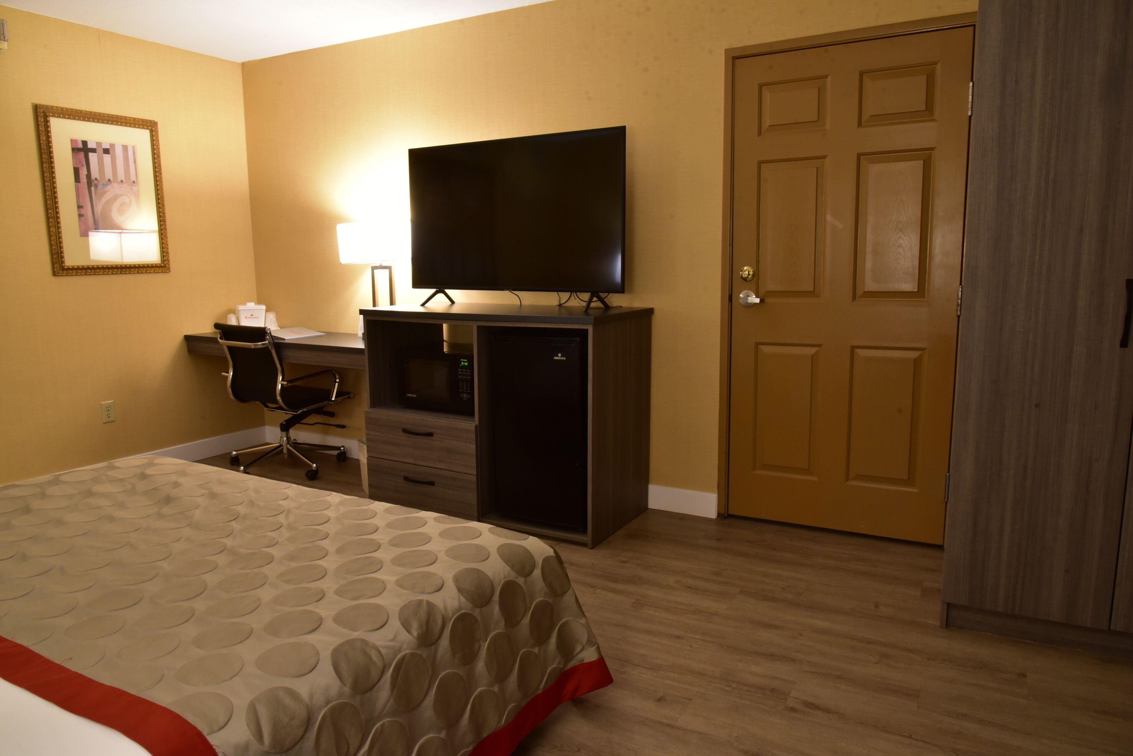 Een hotelkamer met een bed, een bureau met een computer, een televisie en een kledingkast.