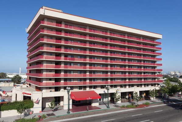 Un hotel de varios pisos con fachada roja y blanca, varios balcones y un área de entrada cubierta.