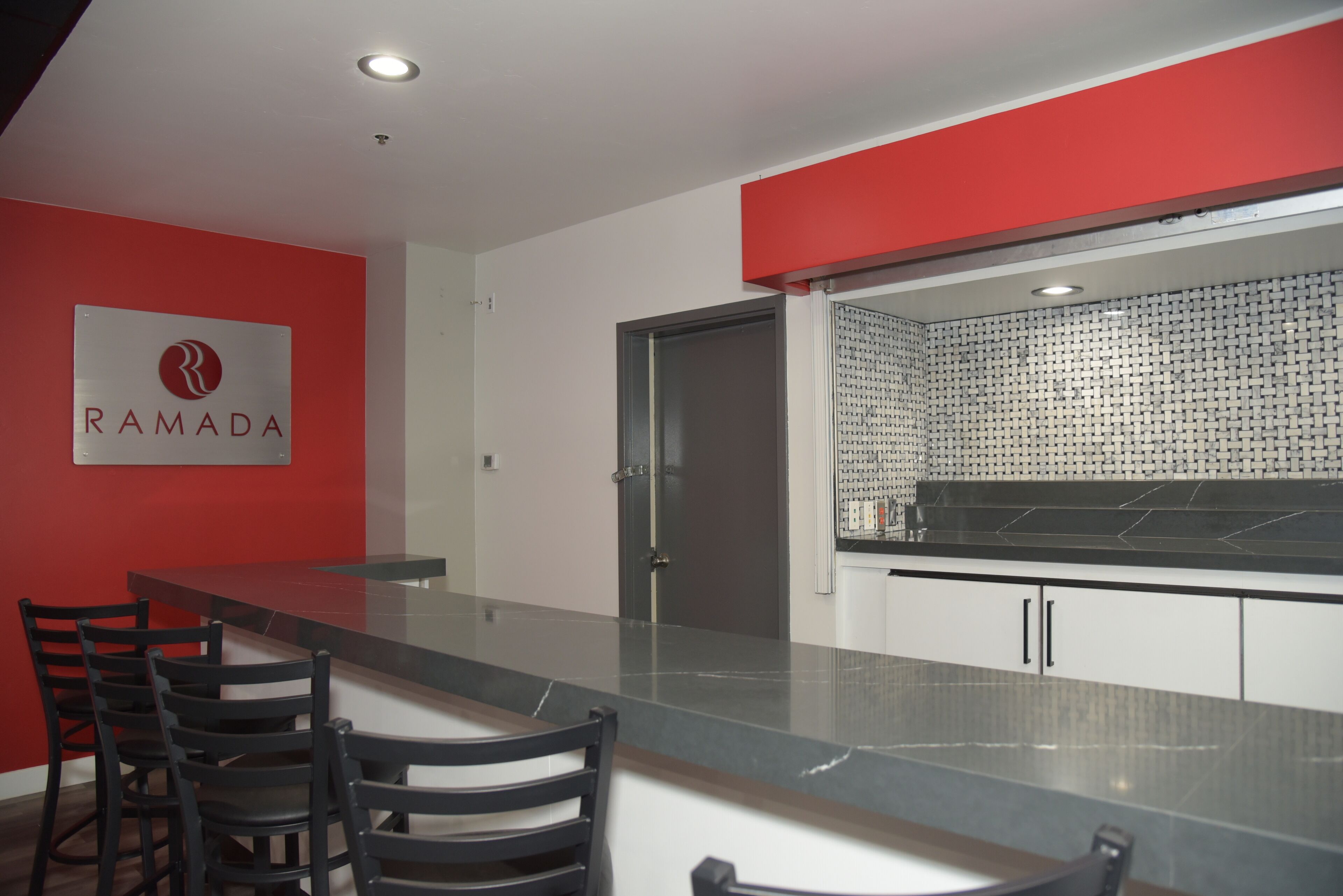 A modern kitchen with a marble countertop, black chairs, and a red accent wall.