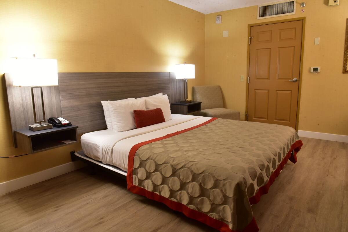 A hotel room with a bed, bedside lamps, a chair, a door, and a nightstand with a phone.