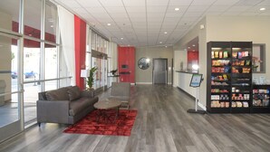 A spacious lobby with a grey sofa, a red rug, and a snack kiosk. - Ramada by Wyndham San Diego National City (National City)