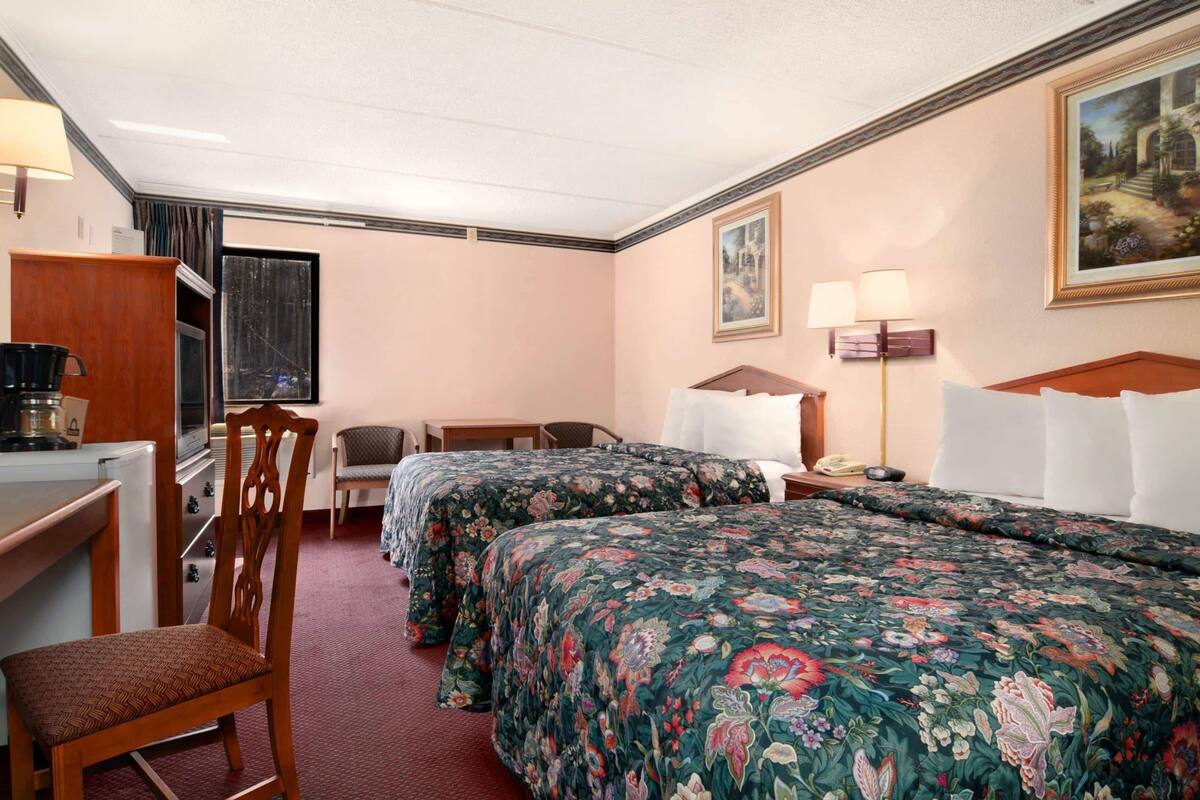 A hotel room with two beds, a desk, a chair, a lamp, and a painting on the wall.