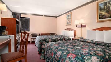 Habitación de hotel con dos camas, un escritorio, una silla, una lámpara y un cuadro en la pared.