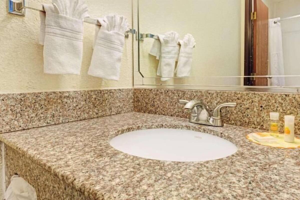 A bathroom with a granite countertop, a white sink, a mirror, and towels hanging on a rack.