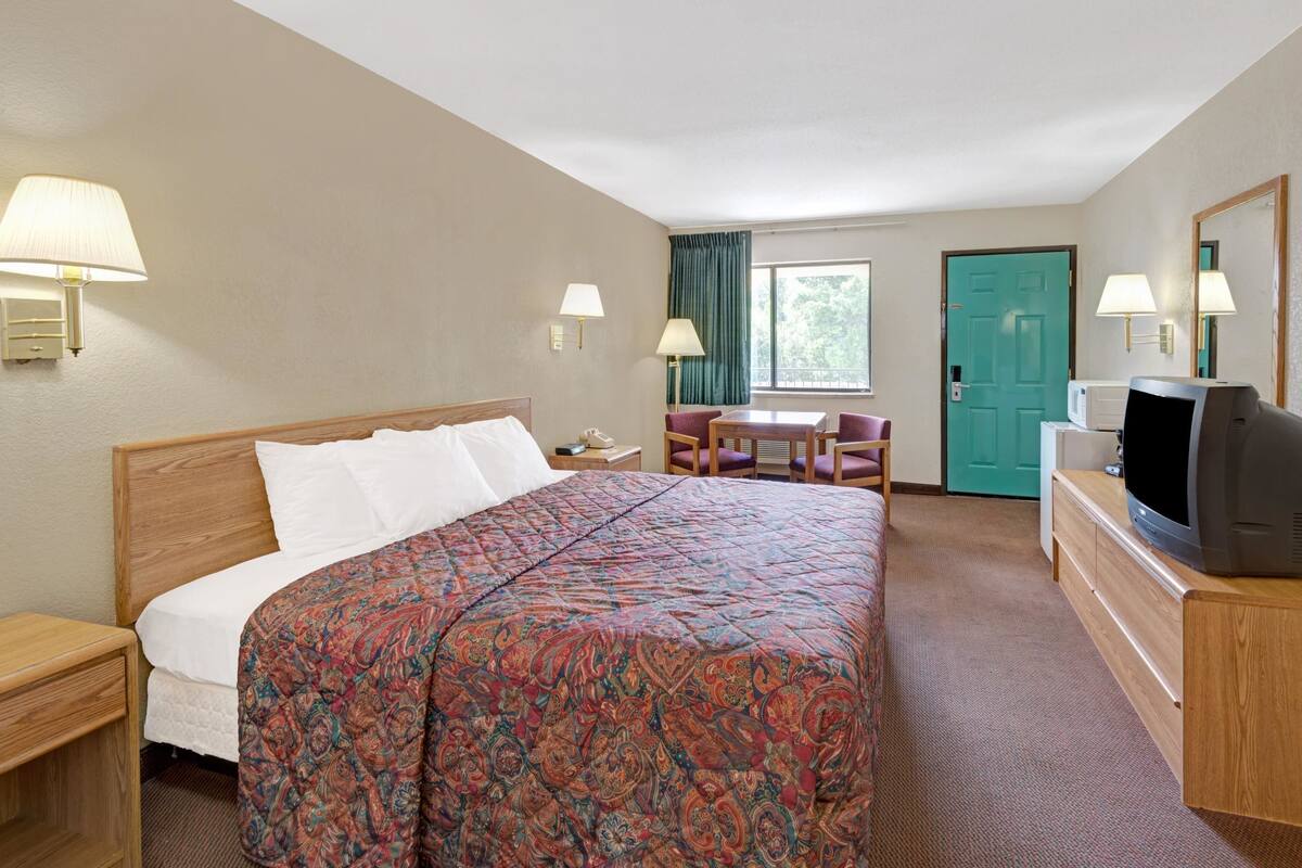 A hotel room with a bed, a desk, a television, and a window with curtains.