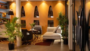 A modern lobby with a sofa, armchairs, a coffee table, a potted plant, and a bookshelf.