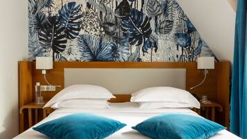 A hotel room with a bed, two pillows, a headboard, bedside tables, and a wall tapestry.