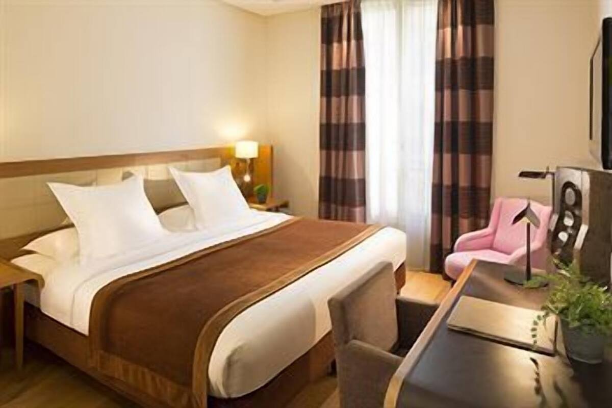 A hotel room with a bed, a desk, a chair, a lamp, and a television.