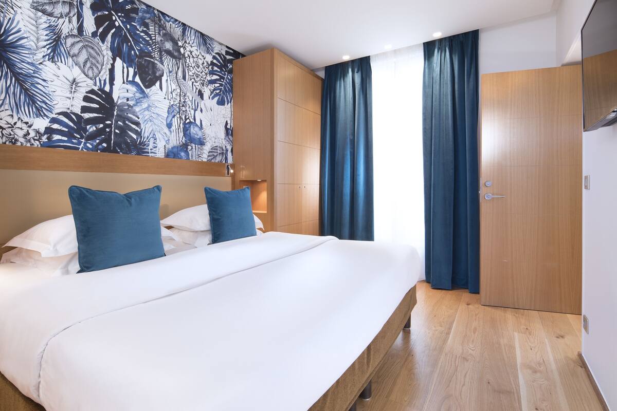 A hotel room with a large bed, wooden headboard, and a tropical leaf-patterned wall.