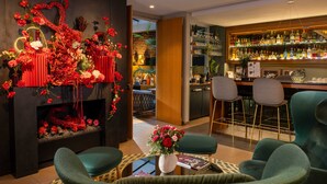 A bar area with a wooden counter and bar stools, a decorative wall with red floral arrangements, and a seating area with green upholstered chairs.