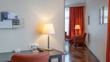 A hotel room with a desk, a telephone, a lamp, a chair, and a dining area with chairs and a table.