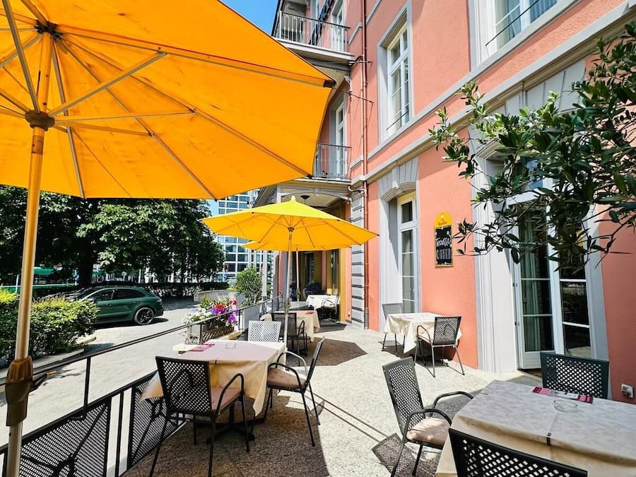 Un patio al aire libre con mesas y sillas, sombrillas amarillas y un edificio con balcones.