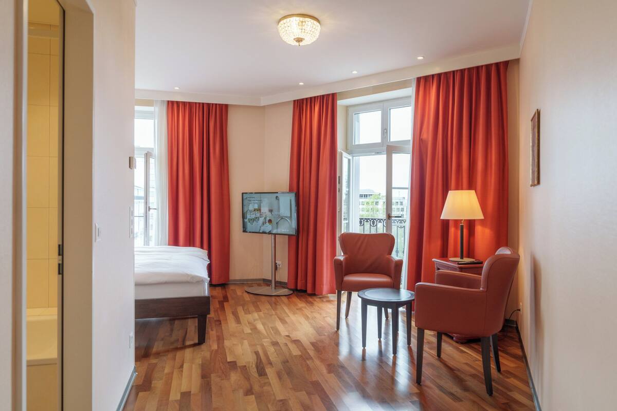 A hotel room with a bed, a TV, a desk with a chair, and a lamp.