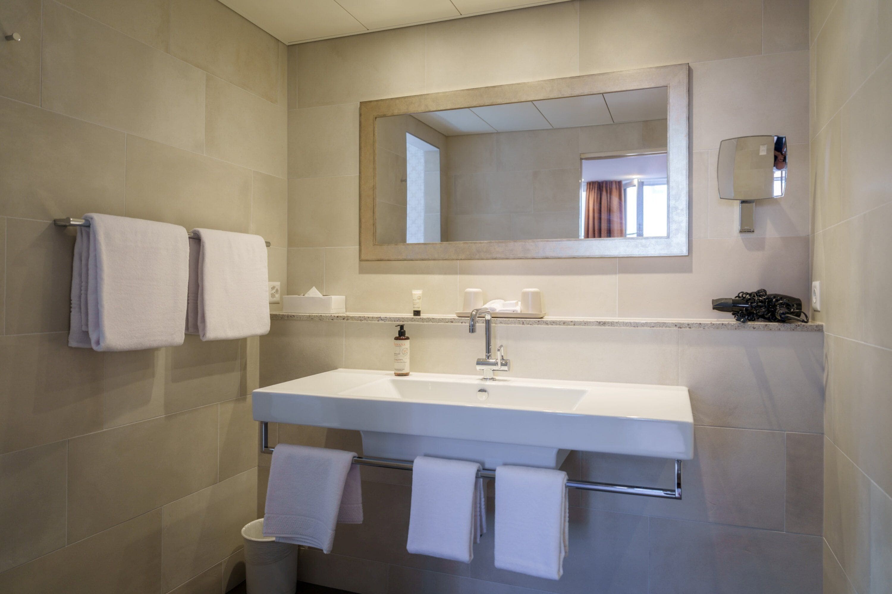 Un baño moderno con un espejo grande, lavamanos blanco y varias toallas.