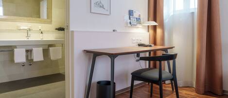 Une salle de bain moderne avec un lavabo, un miroir et un porte-serviettes. On y trouve également un bureau avec une chaise et une poubelle.