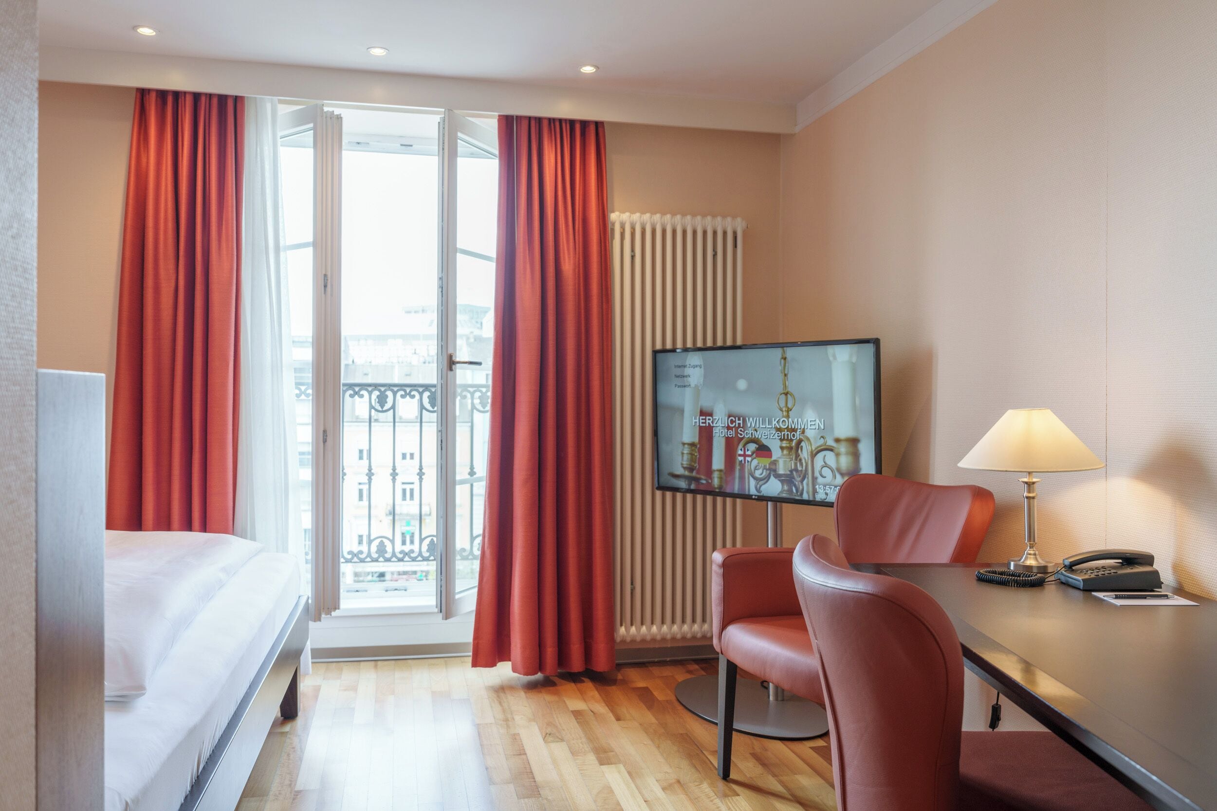 Une chambre d’hôtel avec un lit, un bureau avec une lampe, une chaise, une télévision et une fenêtre avec des rideaux.