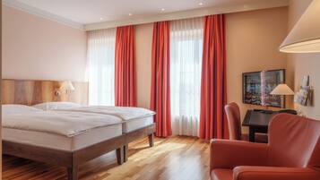 Una habitación de hotel con una cama de madera, cortinas rojas, un escritorio con lámpara y una silla.