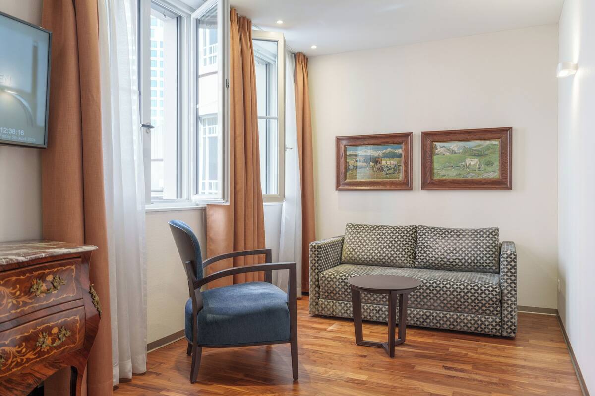 A room with a wooden floor, a patterned sofa, a blue chair, a small round table, and two framed pictures on the wall.