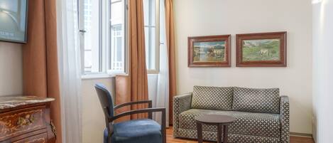 A room with a wooden floor, a blue chair, a patterned sofa, a small table, and two framed pictures on the wall.
