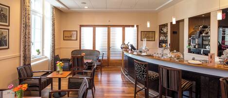 A hotel lobby with a bar area, seating arrangements, and a view through a glass door.