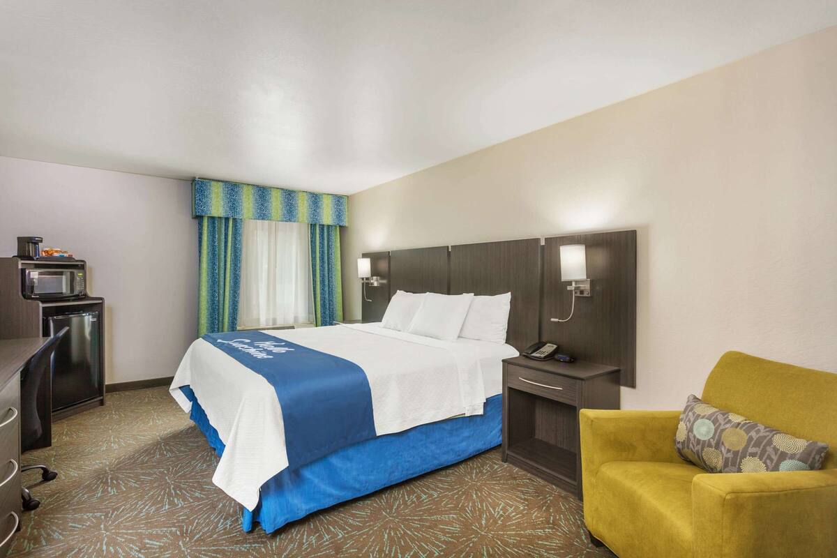 Una habitación de hotel con cama, escritorio, silla y mesita de noche con lámpara.