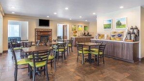 A dining area with multiple tables and chairs, a kitchen counter with various appliances, and a television mounted on the wall.