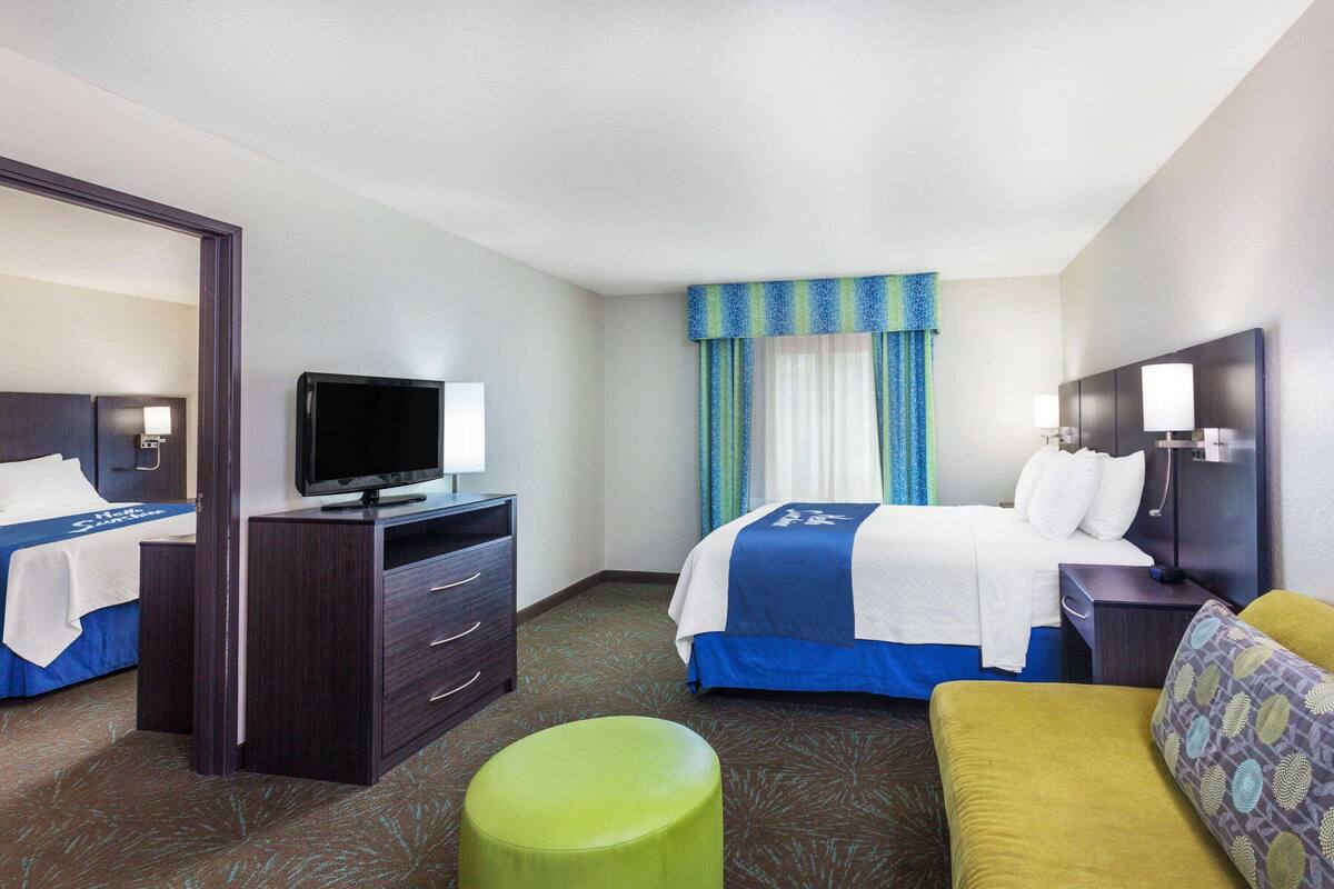 Habitación de hotel con dos camas, un televisor, un escritorio y un taburete verde.
