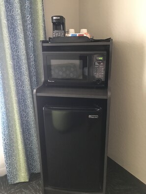 Een kleine keuken met een magnetron en een kleine koelkast, een koffiezetapparaat, en een aantal verpakte etenswaren erboven.