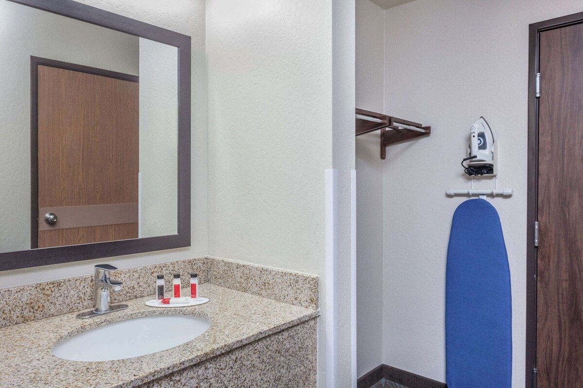 Baño con lavamanos, espejo y tabla de planchar.
