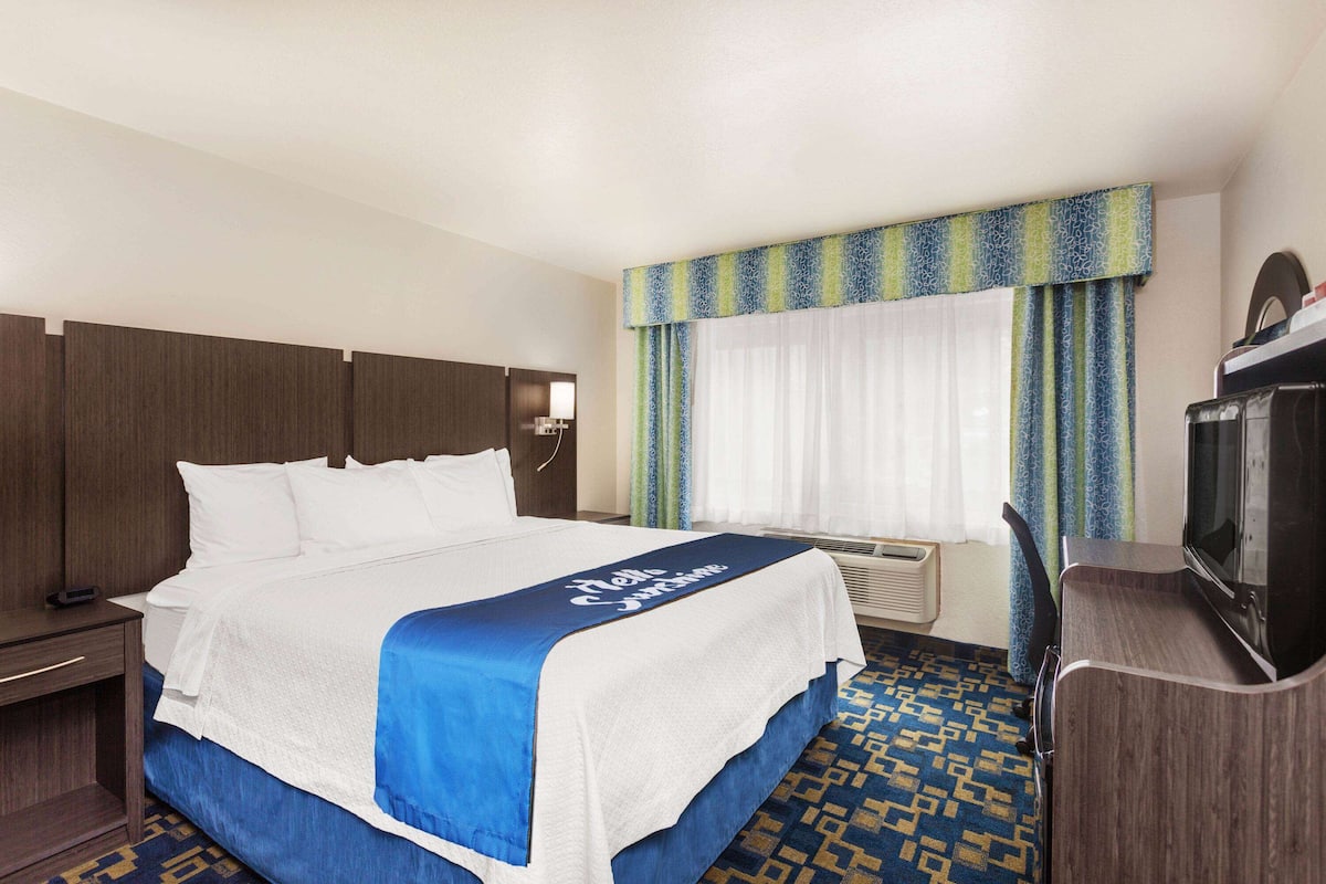 Una habitación de hotel con cama, escritorio, televisor y ventana con cortinas.