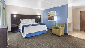 A hotel room with a bed, a nightstand, a chair, a lamp, and a painting on the wall.