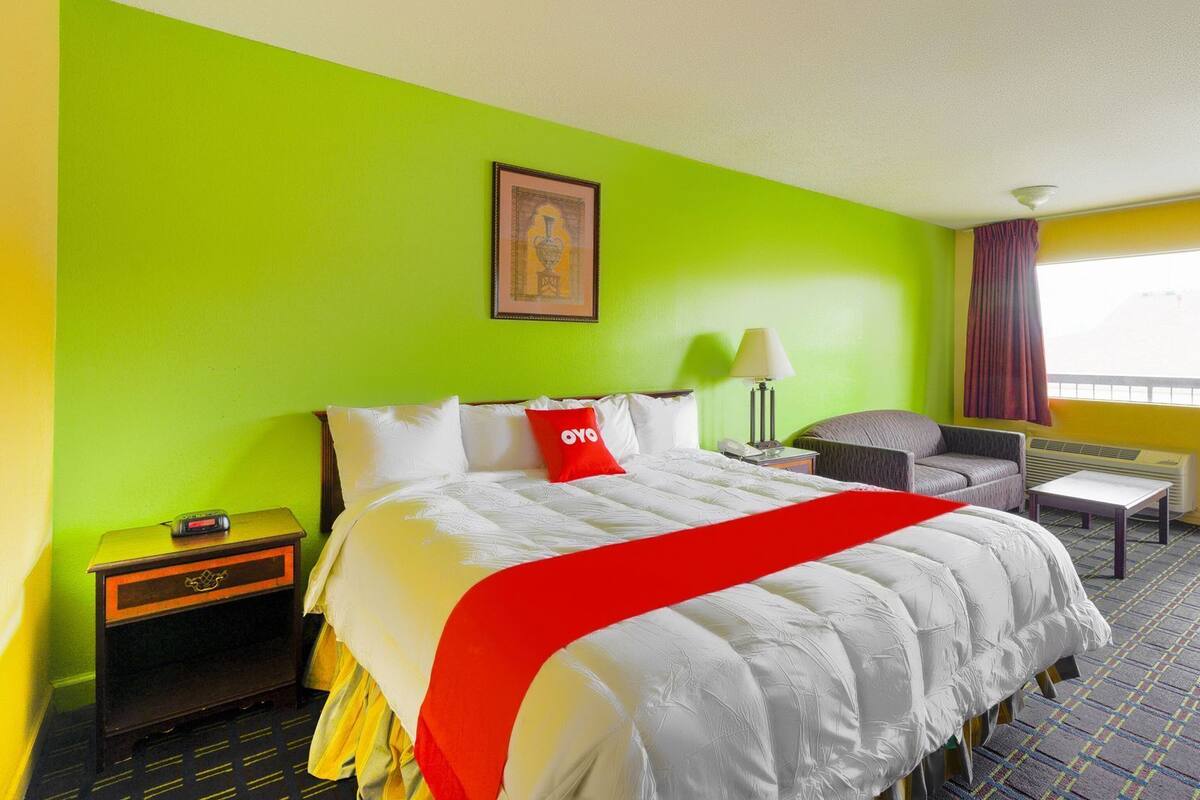 A hotel room with a bed, a chair, a desk, and a window.