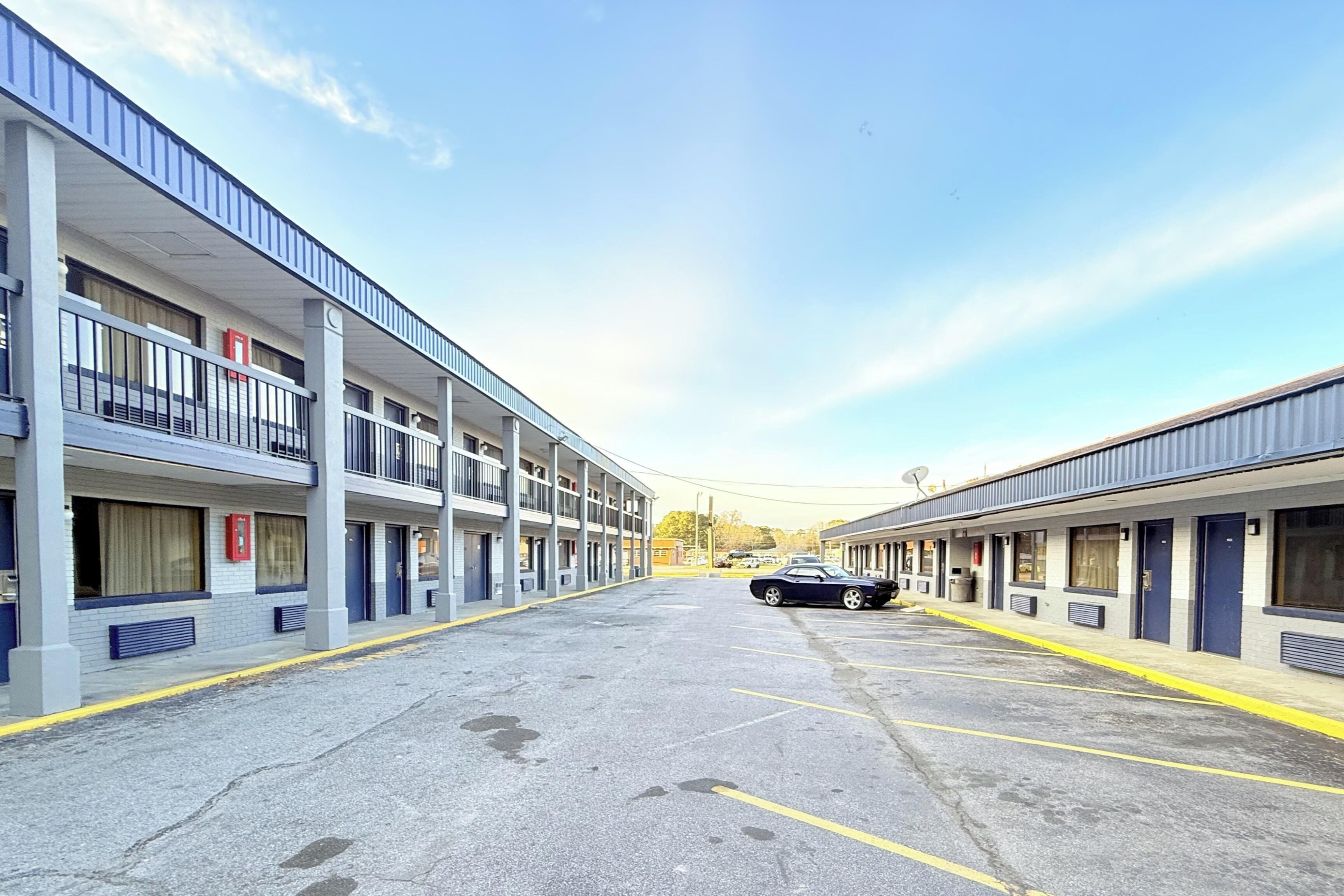 A multi-story motel with a central parking area and a car parked in the lot.