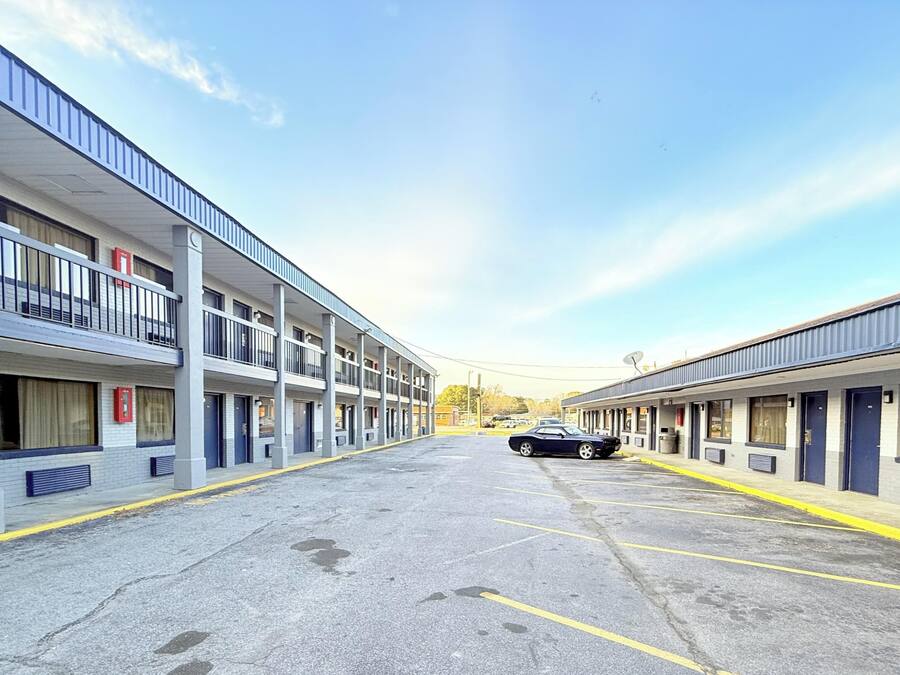 A multi-story motel with a central parking area and a car parked in the lot.