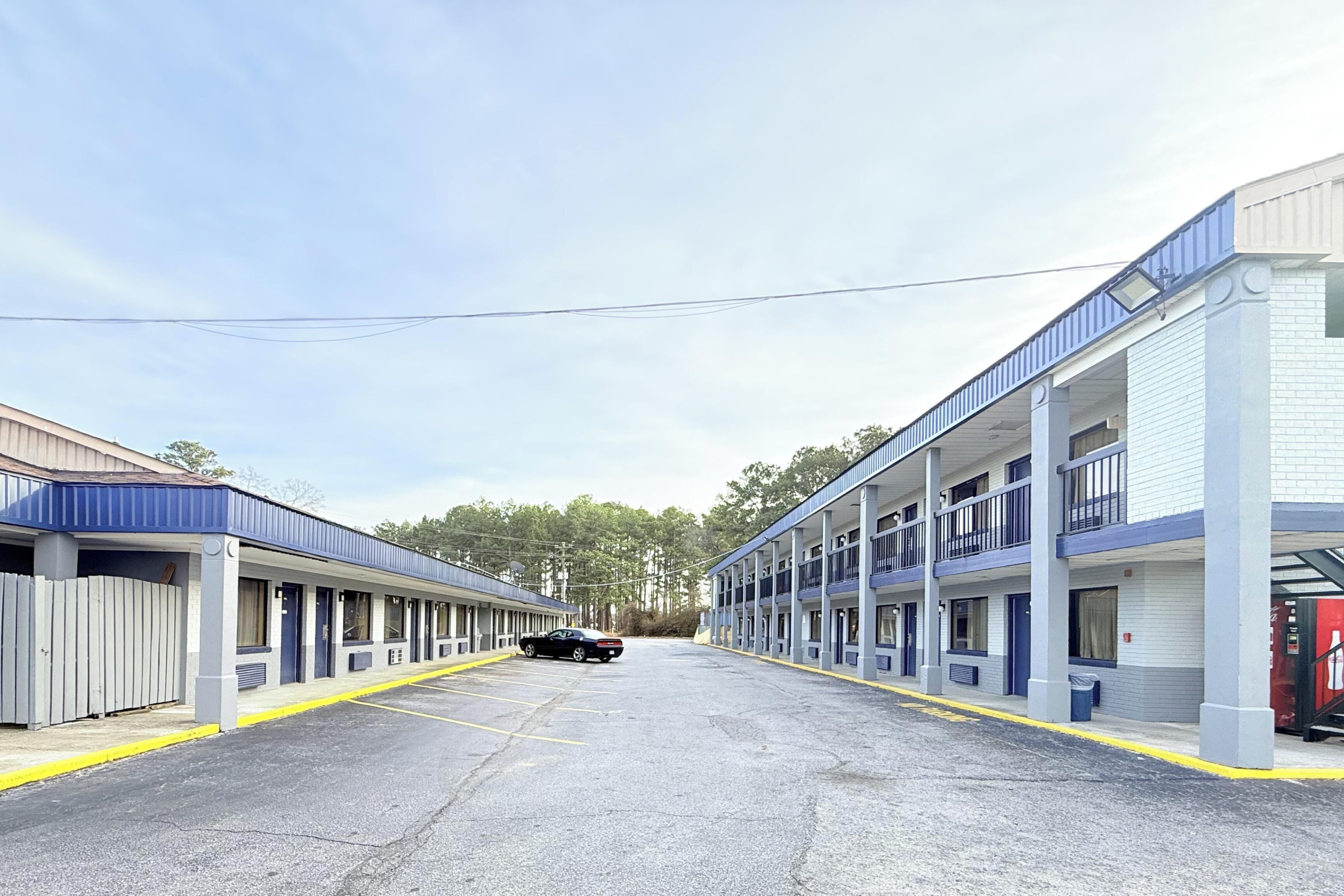 A motel with a row of rooms, a parking lot, and a black car parked in the lot.