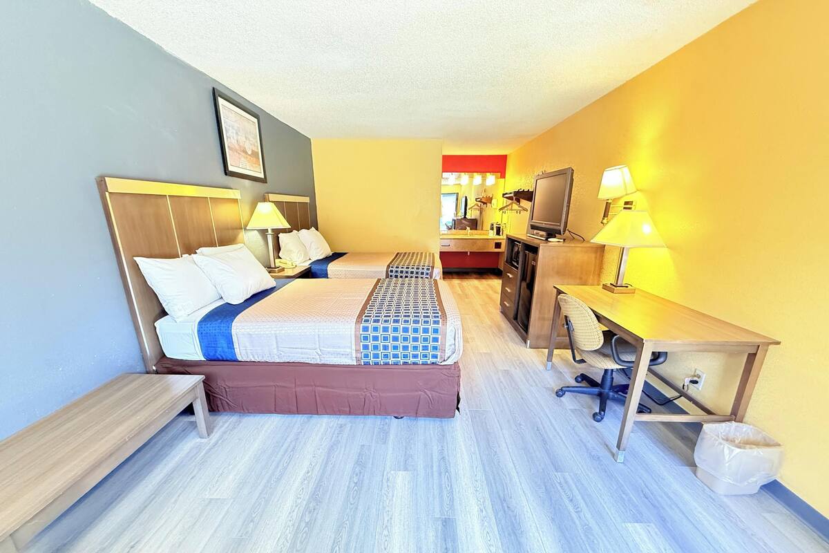 A hotel room with a bed, desk, chair, TV, and a small kitchenette.
