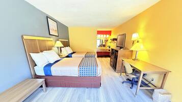 Habitación de hotel con cama, escritorio, silla, televisión y una pequeña kitchenette.